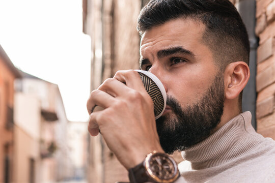 Close-up image of a bearded man in a turtleneck sweater sipping coffee from his portable mug.