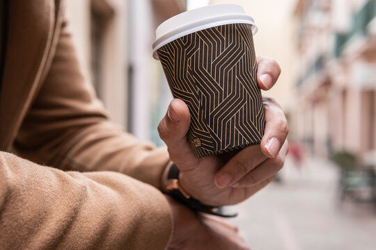 Close-up image of a man's hand holding his disposable cup of tea or coffee in a beautiful central street.