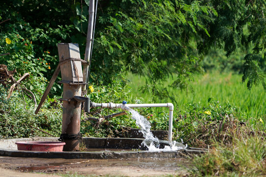Water flow from pumping pipe and Old hand operated water pumping rural India high water pressure with trees and greenery in background