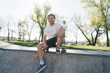Young sportsman sitting on skateboard on ramp in skate park