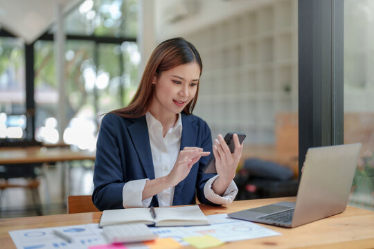 Happy Asian businesswoman working with a smile and using her smartphone for business communication respond to chats and talk to various LINE applications in the office.