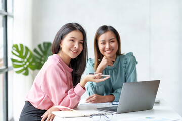 Two Asian businesswoman talk, discuss, work together to exchange ideas, presenting new start-up project ideas analyze marketing plans and office investments.