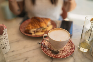Chica joven guapa morena desayunando croissant relleno en cafeteria estilo cozy