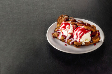 Hong Kong chocolate bubble waffle with ice cream and strawberry or raspberry syrup on dark background with copy space.