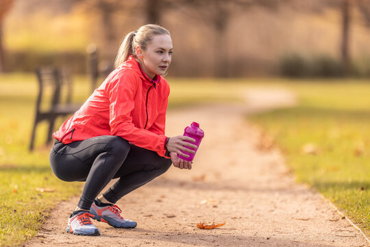 A resting sportswoman holds a plastic bottle with a drink in her hand after running in the park