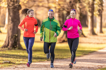 A trio of runners, two young women and one mature man are running in an autumn park