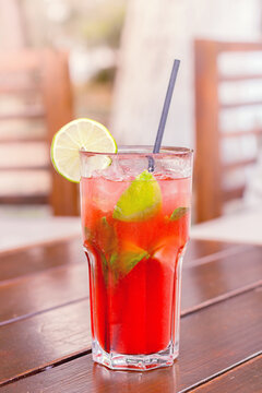 Red cocktail in glass shooted above wooden table.