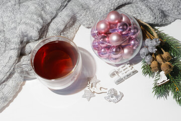 Obraz na płótnie Canvas Christmas arrangement of pink balls for the Christmas tree, cups of black tea, decorated with a knitted gray sweater on a white table. Preparation for the holidays. Lubrication effect