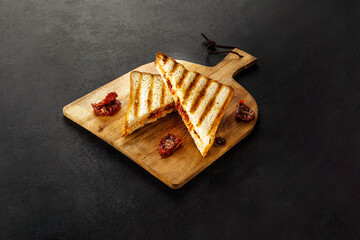 Club sandwich with dryed tomatoes on wooden board.