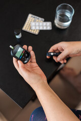 Woman measures blood sugar glucose meter, diabetes concept, notebook for writing and monitoring. Woman write blood glucose level from glucose meter, medical consultation and examination in hospital.