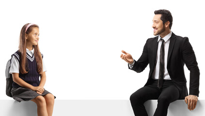 Professional man sitting on a blank panel and talking to a schoolgirl