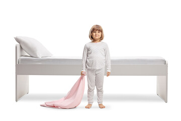 Full length portrait of a little girl in pajamas holding a pink blanket in front of a bed