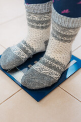 A woman in gray warm socks stands on the scales, weighs herself after gluttony during the holidays