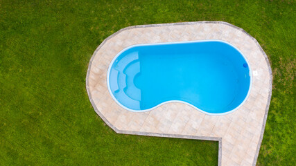 Aerial view of a swimming pool with wavy and curved shapes. Around the pool is a lawn with grass. Vacation house concept.