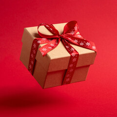Flying Christmas gift box with red bow on red background.