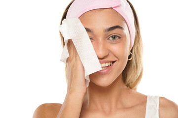 Attractive smiling young woman cleaning her face with a wet tissue on a white background