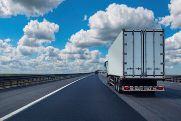 Truck is driving on highway. Transportation of goods by truck. Truck back view. Lory in summer weather. Transport business concept. Freight company services. Lory with white container under blue sky