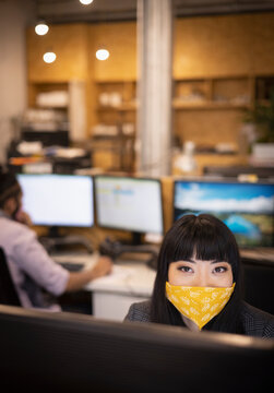 Portrait confident businesswoman in face mask at computer in office