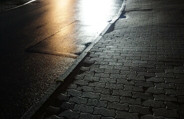 Nasser Bürgersteig mit grauen Pflastersteinen und nasse Straße mit weißen und goldbraunen...