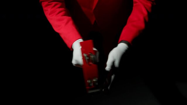 A musician in a black room plays the tambourine. He's wearing a red suit