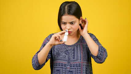 Sick unhealthy ill allergic young woman holding nasal drops or nose drop bottle isolated over yellow background