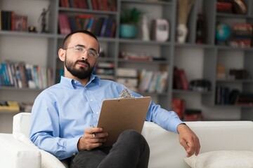 Male psychoanalyst sitting on sofa with clipboard.