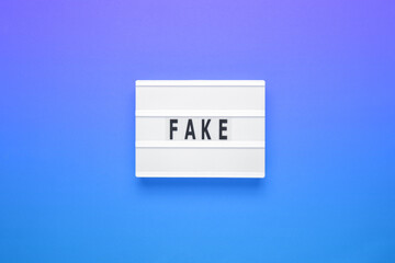Lightbox with word fake on blue background. Business, fake and fact concept.