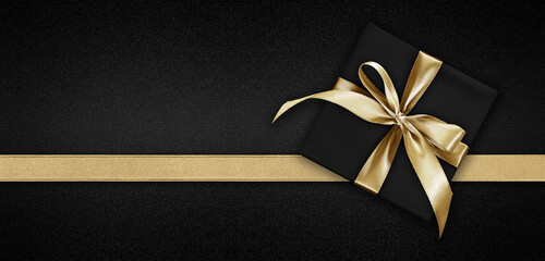 Blank gift greeting card with gift box present and bright shiny golden ribbon bow tape isolated on black background, top view and copy space for merry Christmas template or shopping advertising banner - obrazy, fototapety, plakaty