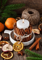 Fototapeta na wymiar Handmade Christmas candle decorated with cinnamon sticks. Slices of fresh dried apple, orange and spices for cooking or baking. Rustic style. Home decoration concept.