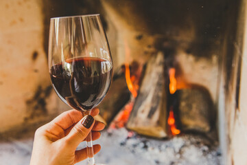 Mão segurando taça de vinho tinto em lareira no inverno
