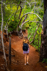 girl with backpack walks through forest on aiea loop trail on oahu; hiking through mountains on hawaii islands near honolulu