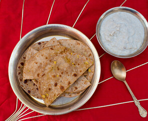 Dal Puri or dal stuffed paratha in brass plate and Gur kheer or kheer made with rice, jaggery and milk in bowl in red background. Bihari thali called kheer puri.