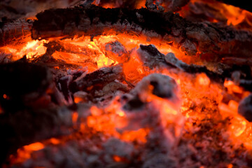 Close up of charcoal embers and ash from a fire glowing red hot with a shallow focus depth of field..