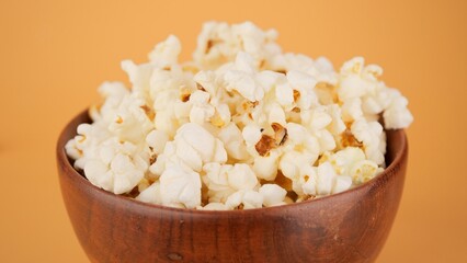 Popcorn in wooden bowl close up, yellow background