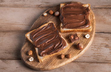 Board of bread with chocolate paste and hazelnuts on wooden background. Popular desser food. Top view.