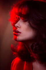 Closeup beauty portrait of young woman with makeup and hairstyle, wear red suit, with closed eyes, red neon studio light.
