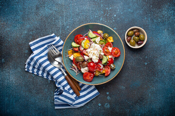 Greek fresh healthy colorful salad with feta cheese, vegetables, olives in blue ceramic bowl on rustic concrete background top view, Mediterranean diet, traditional cuisine of Greece 