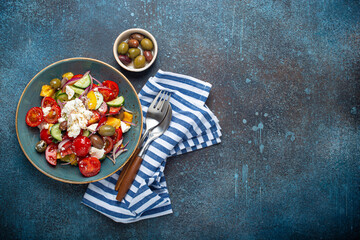 Greek fresh healthy colorful salad with feta cheese, vegetables, olives in blue ceramic bowl on rustic concrete background top view, Mediterranean diet, traditional cuisine of Greece. Space for text