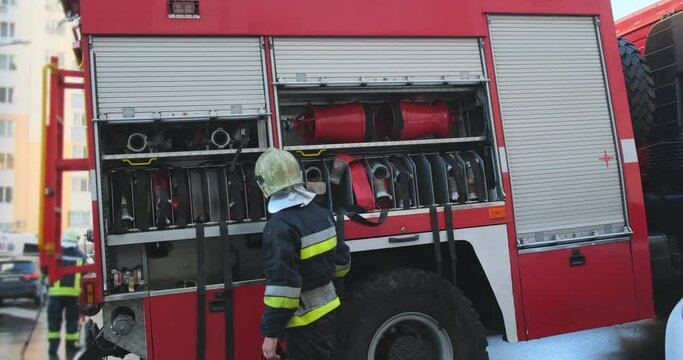 Uniformed fireman closes a roller shutter on the side of a fire engine. The end of the working day, the fire is extinguished. The concept of finishing a dangerous job.