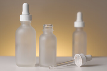 Three empty white translucent glass dropper vials, one open, one blurry. Different-sized bottles  against warm yellow backdrop. Horizontal beauty background and copy space. Professional lighting.