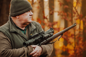 Fototapeta premium Portrait of hunter or ranger with gun or rifle in the forest looking out or hunting of some venison, hunting period, autumn season, hunting and people concept