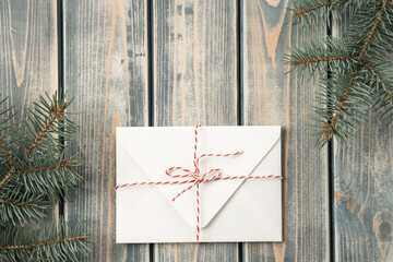 White envelope on on gray wooden background with branches of Christmas tree tied with cord with bow. Top view