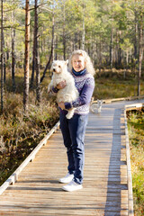 Obraz premium Woman with West Highland white terrier standing in autumn sun. Woman has Icenlandic pullover 