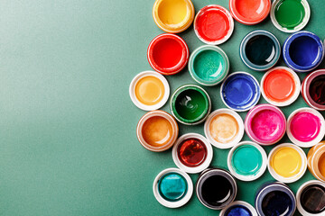 Beautiful, bright, mother-of-pearl, multicolored open cans of paint on a green background. View from above. The concept of creativity.