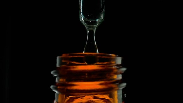 Drop of clear liquid, oil, serum or tincture dripping from pipette in the neck of a brown medical bottle. Macro shot of dripping drops of essential oil on black background.