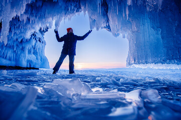 Tourist man in Ice blue cave or grotto on frozen lake Baikal. Adventure winter landscape with people