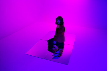 Full length photo of an attractive brunette model in red suit ang black jeans in mixed neon light, posing down on mirror on the floor.