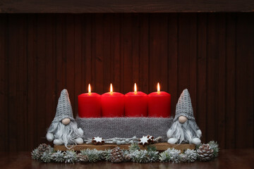 Vier rote brennende Kerzen mit lustigen Weihnachtswichtel vor einem Holzhintergrund.