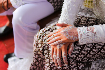 Traditional Sundanese Bride with white nail art and white kebaya dress sitting beside her husband...