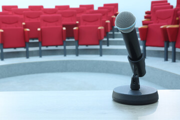 Black microphone with cord against empty seats in lecture room concept photo. Lecturer speaker show...